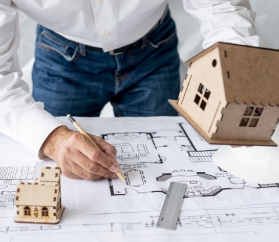 Arquitecto trazando un plano junto a maquetas de vivienda en madera