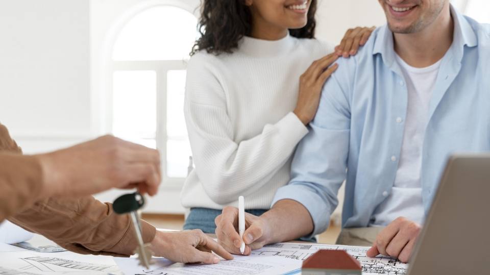 Pareja firmando el contrato de su nueva vivienda mientras reciben las llaves